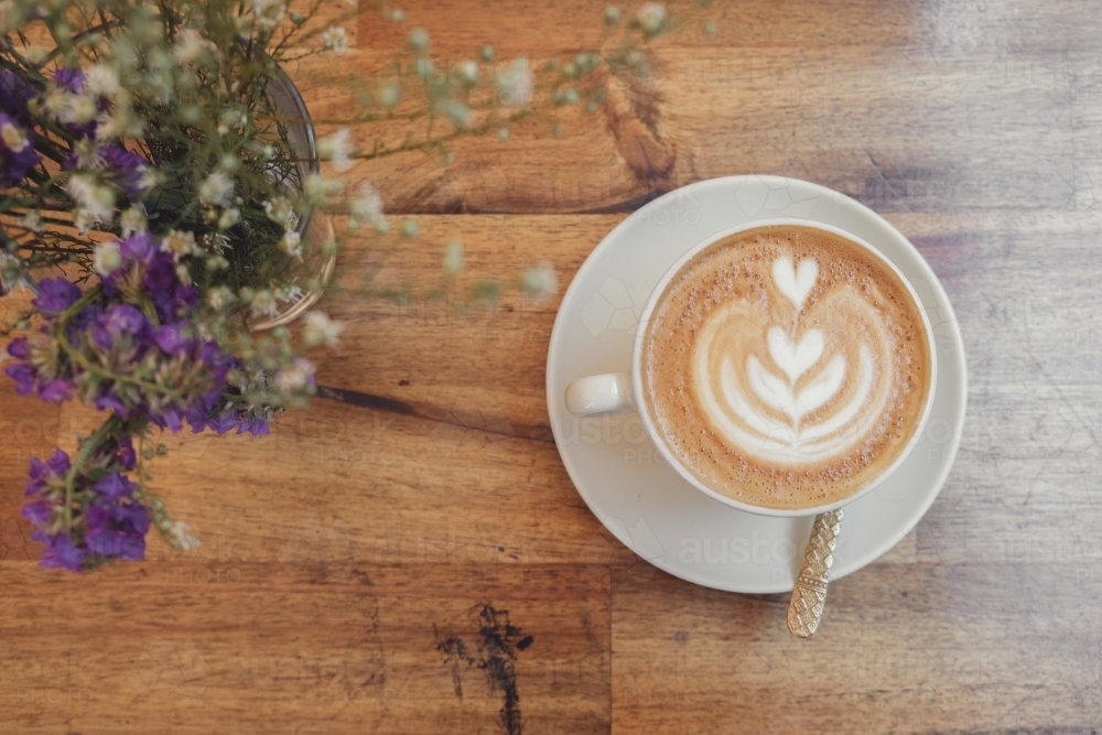 Cup of coffee latte art and flowers on wooden table - Australian Stock Image
