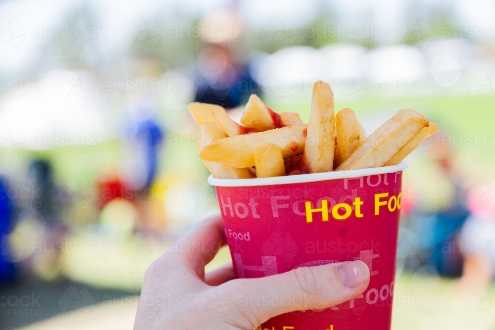 Cup of hot chips and tomato sauce held in hand at sports event - Australian Stock Image