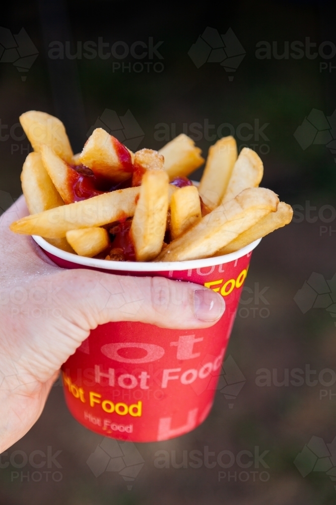 Cup of hot chips and tomato sauce held in hand at sports event - Australian Stock Image