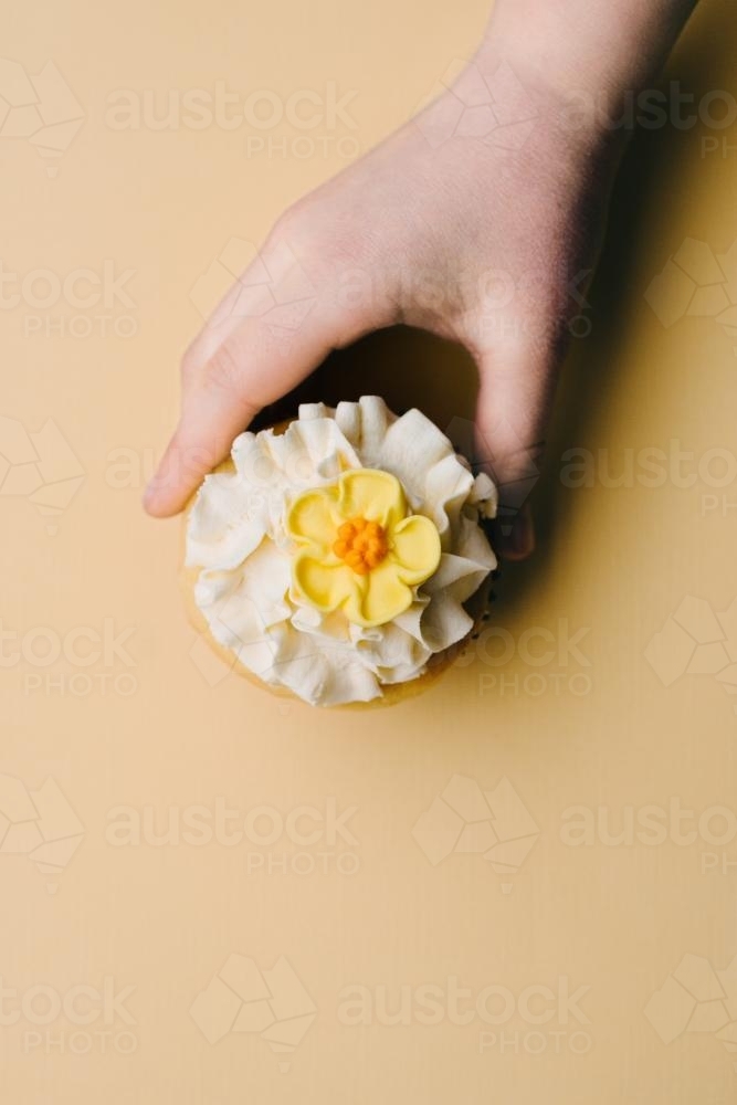 cupcake on yellow background with yellow flower and hand reaching - Australian Stock Image