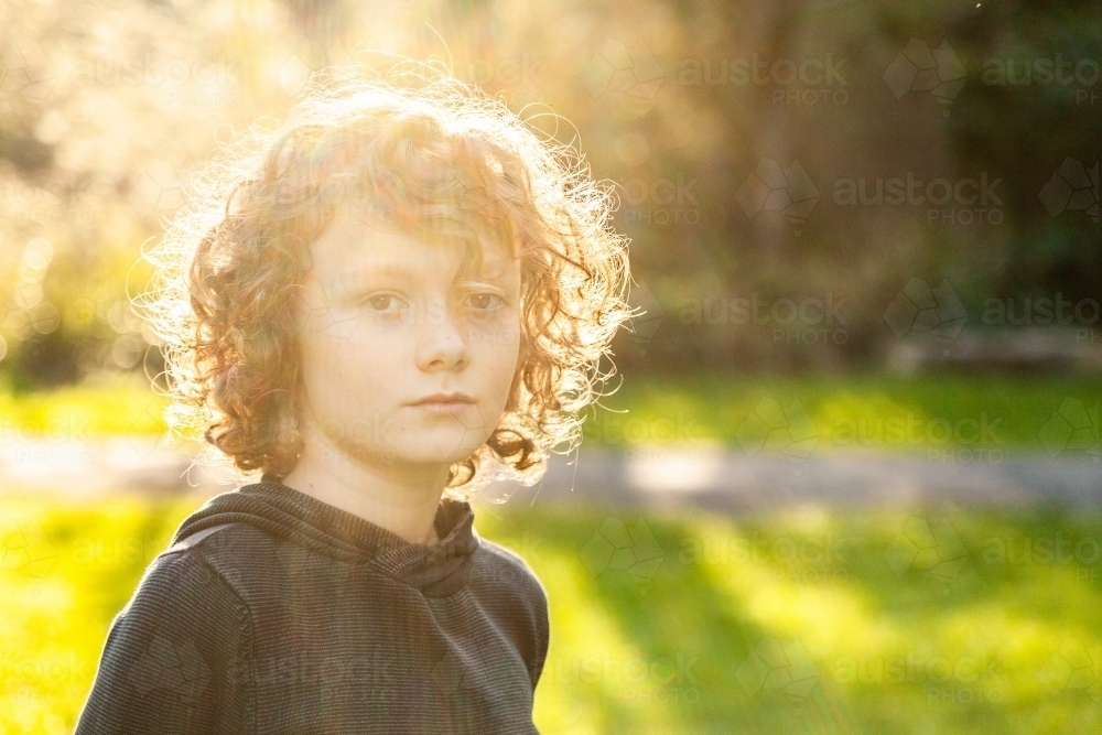 Curly hair boy in sun flare in park - Australian Stock Image