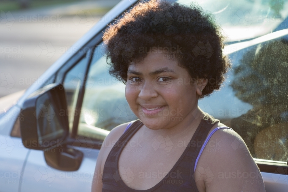 Curly haired kid standing beside car - Australian Stock Image