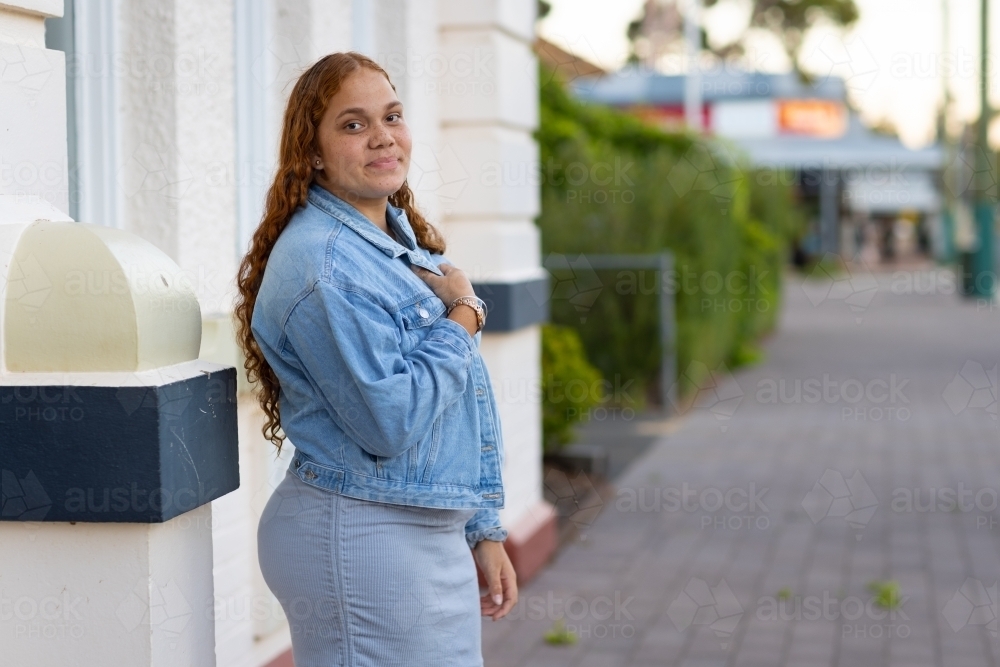 curvy teenage girl with long hair standing alone on footpath - Australian Stock Image