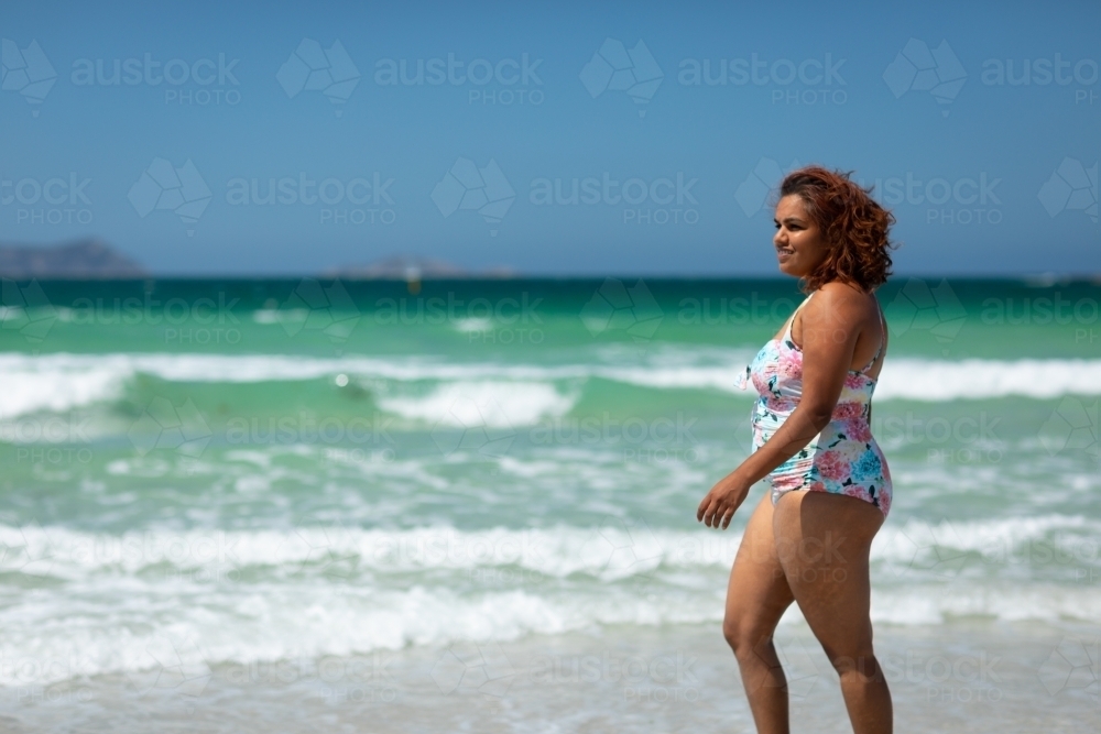 curvy woman walking along the shore on a sunny day - Australian Stock Image