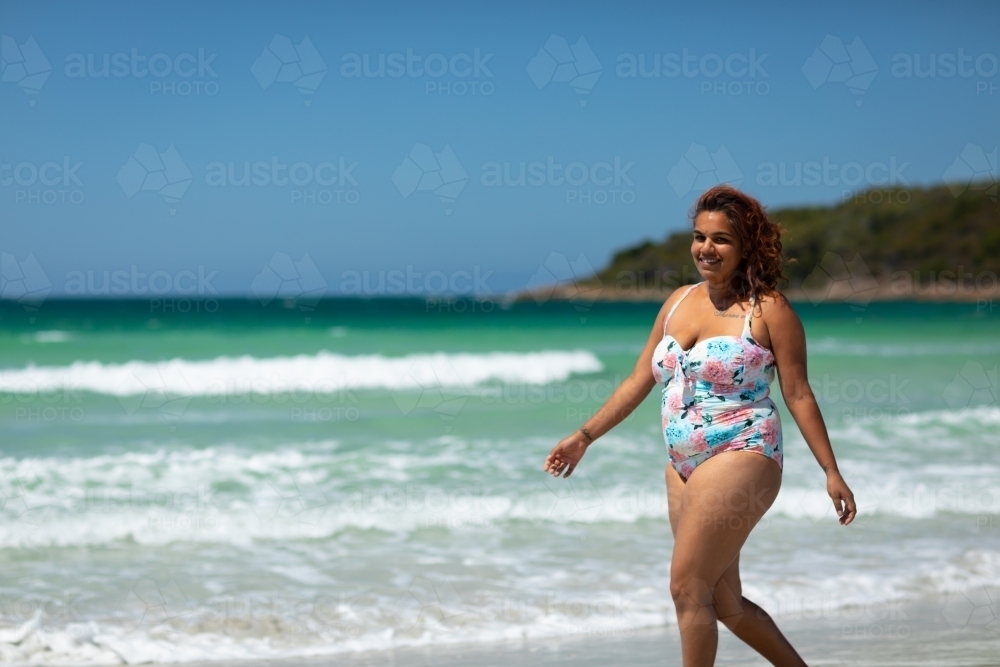 curvy woman walking along the shore on a sunny day - Australian Stock Image