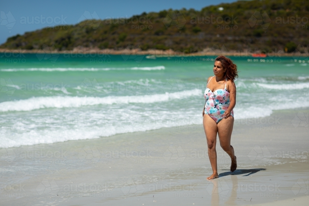 curvy woman walking along the shore on a sunny day - Australian Stock Image