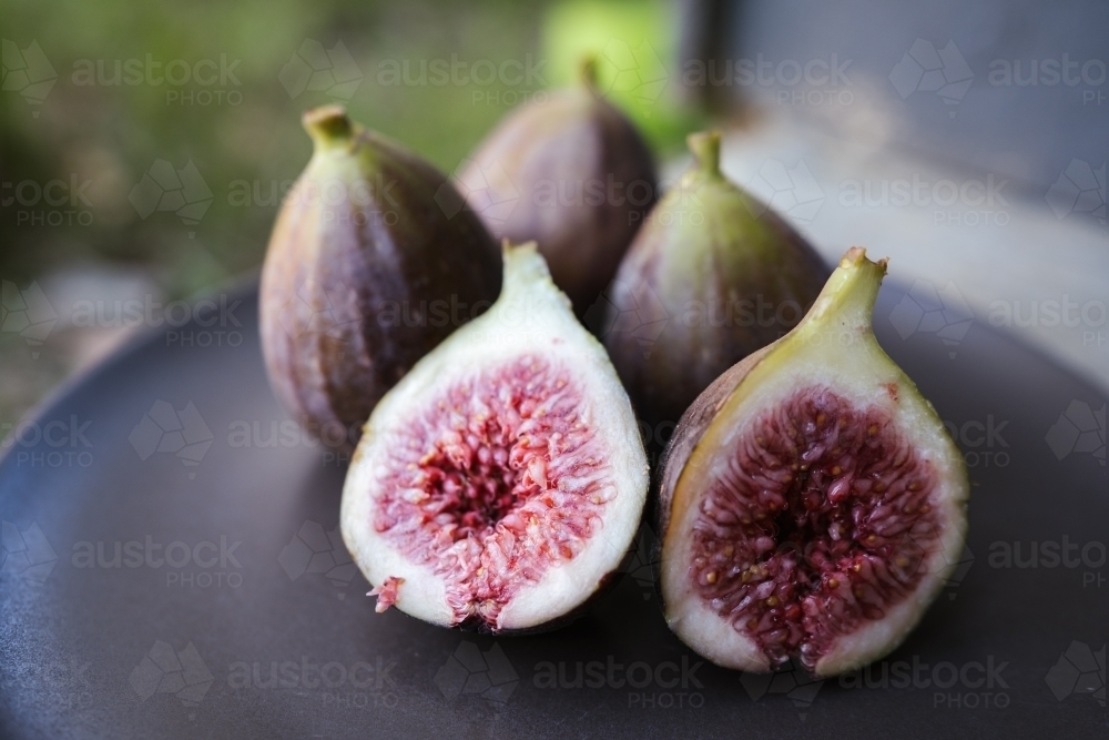 Cut figs on a dark coloured plate - Australian Stock Image