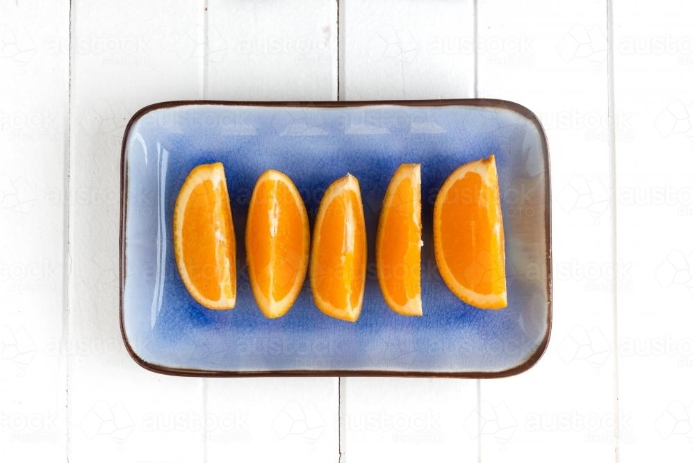 cut orange segments on a blue plate - Australian Stock Image