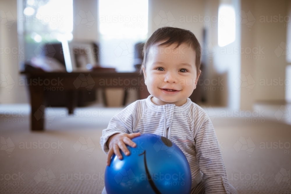 Cute 1 year old mixed race boy plays at home with a smiley face ball - Australian Stock Image