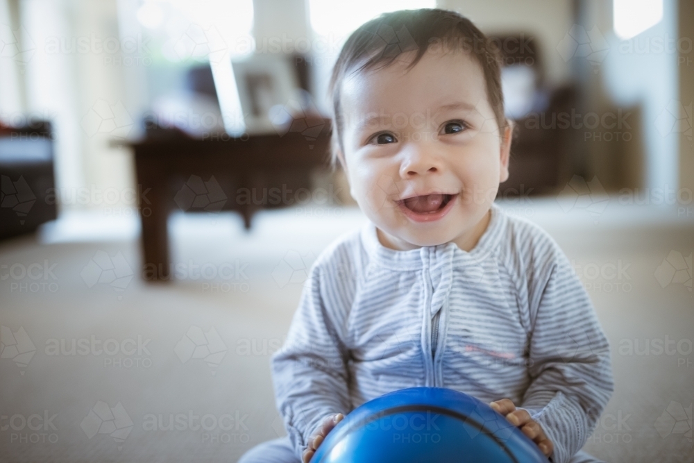 Cute 1 year old mixed race boy plays at home with a smiley face ball - Australian Stock Image