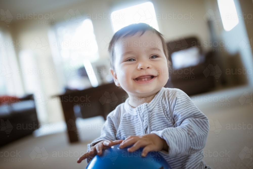 Cute 1 year old mixed race boy plays at home with a smiley face ball - Australian Stock Image