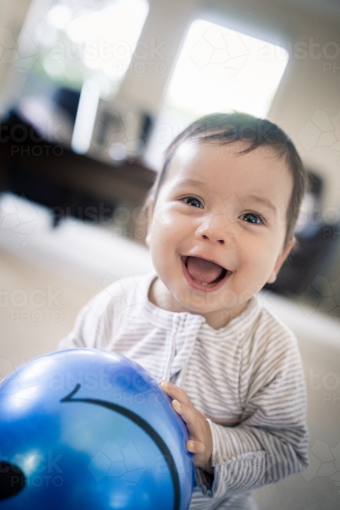 Cute 1 year old mixed race boy plays at home with a smiley face ball - Australian Stock Image
