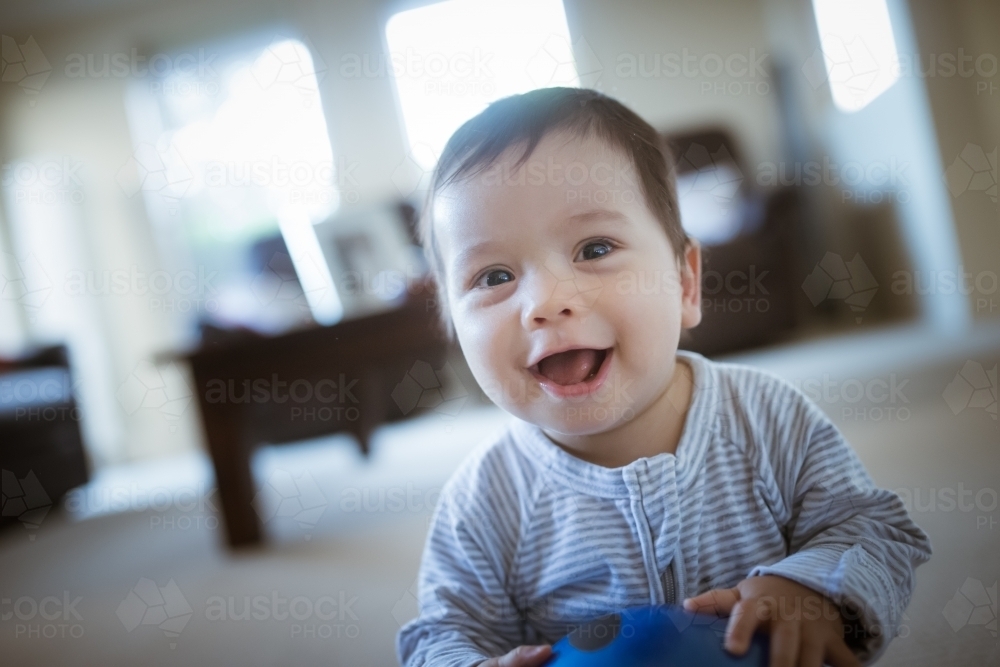 Cute 1 year old mixed race boy plays at home with a smiley face ball - Australian Stock Image