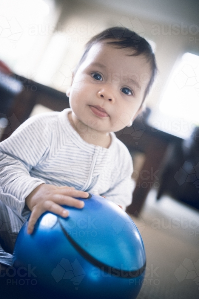 Cute 1 year old mixed race boy plays at home with a smiley face ball - Australian Stock Image