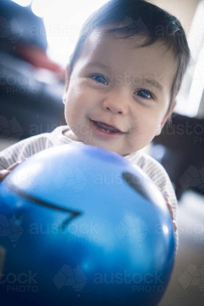 Cute 1 year old mixed race boy plays at home with a smiley face ball - Australian Stock Image