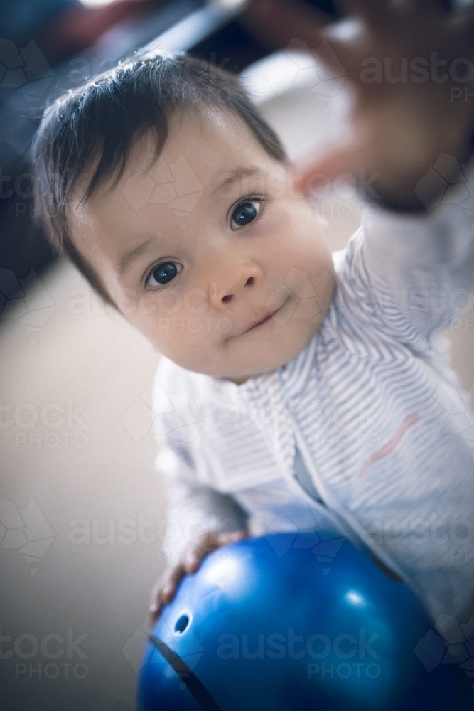 Cute 1 year old mixed race boy plays at home with a smiley face ball - Australian Stock Image