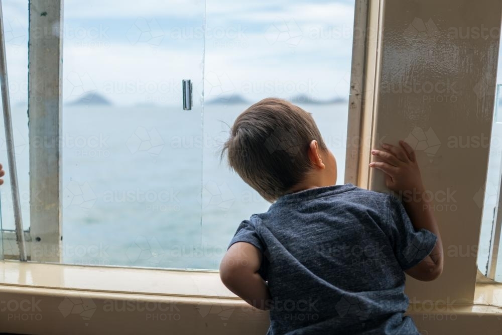 Cute 3 year old mixed race boy looks out a boat window - Australian Stock Image