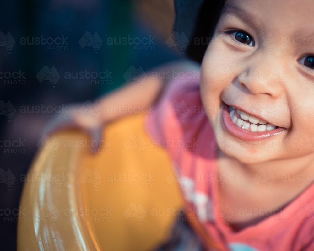 Cute 3 year old mixed race boy plays cheerfully on a playground slide - Australian Stock Image