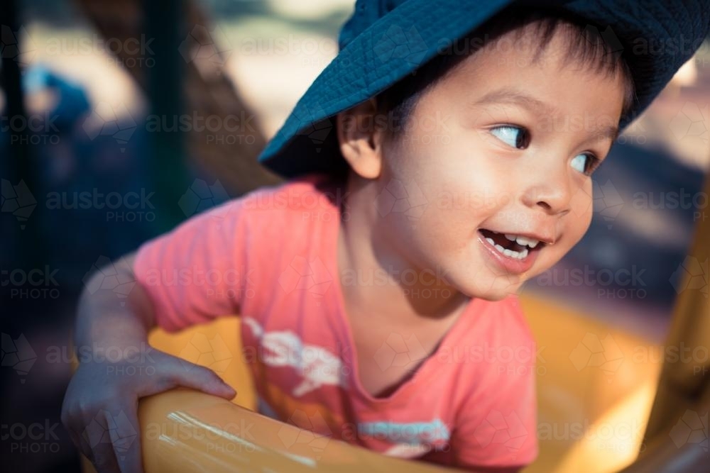 Cute 3 year old mixed race boy plays cheerfully on a playground slide - Australian Stock Image