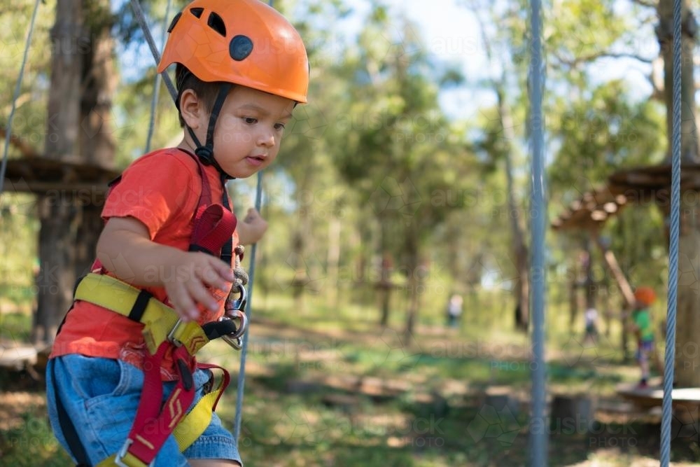 Cute 3 year old mixed race boy plays on an adventure ropes course - Australian Stock Image