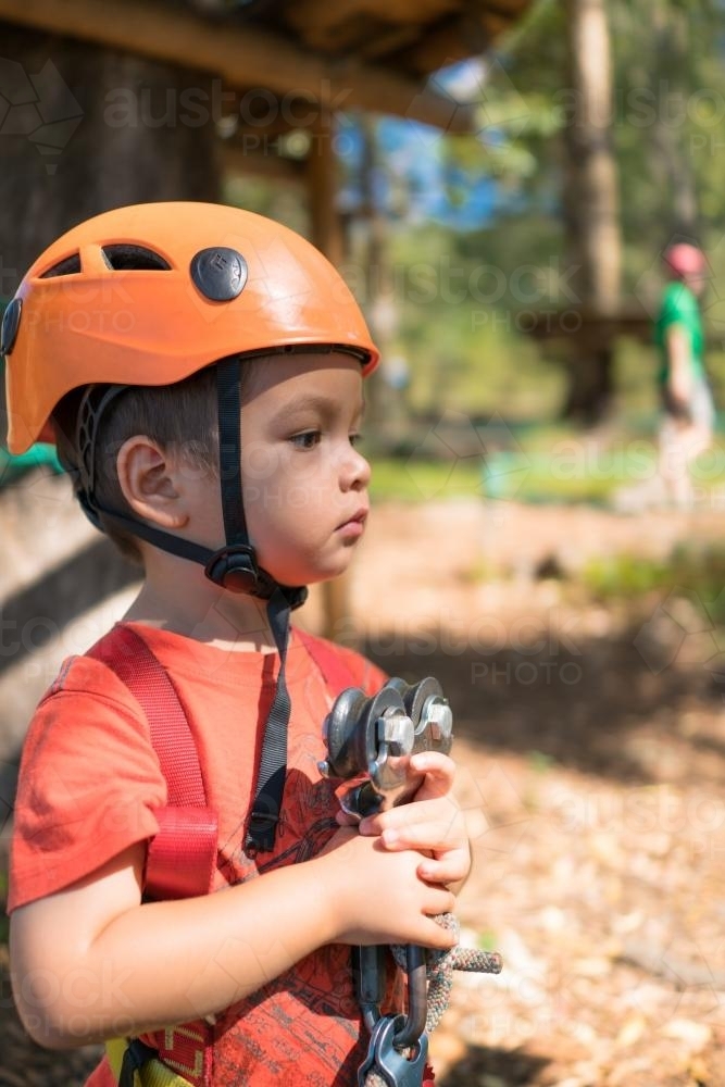Cute 3 year old mixed race boy prepares to play on an adventure ropes course - Australian Stock Image