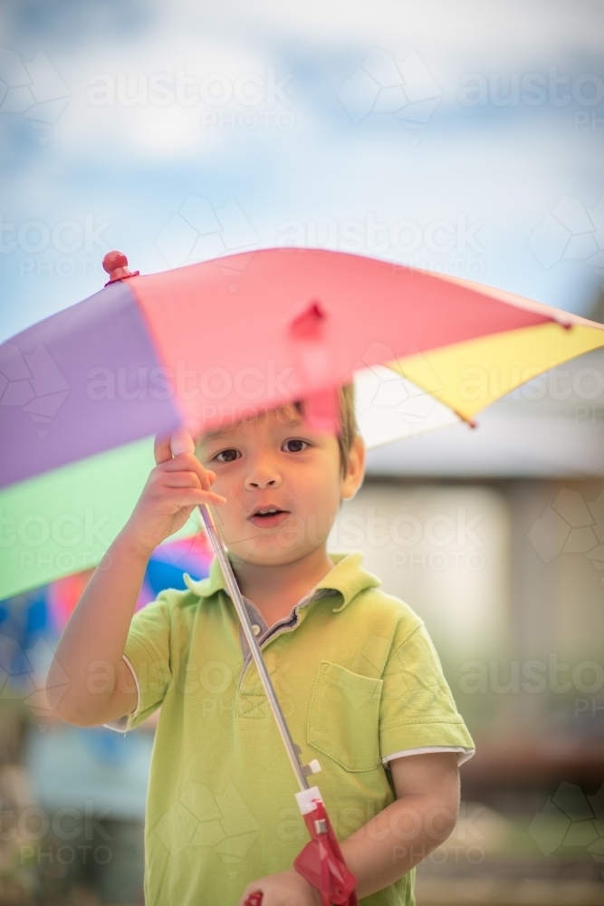 Cute boy plays outside with a rainbow umbrella in a suburban backyard - Australian Stock Image