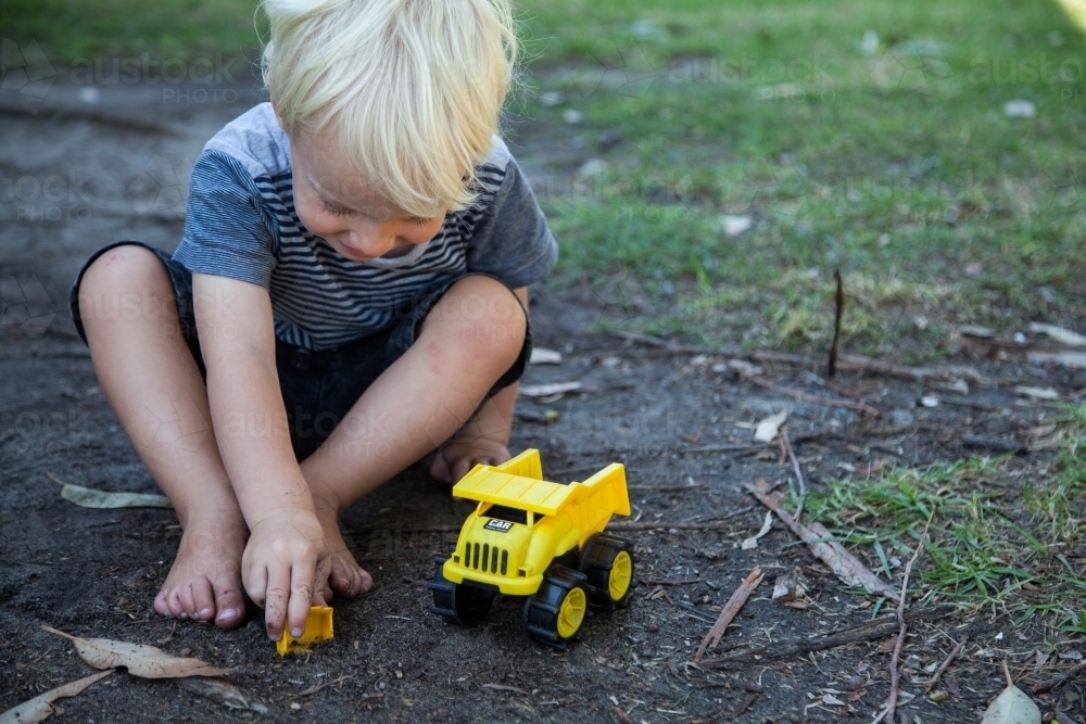 Image of Cute little boy happily playing in black dirt with yellow toy