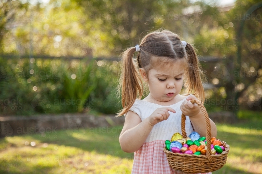 Cute little girl counting coloured Easter eggs in basket - Australian Stock Image