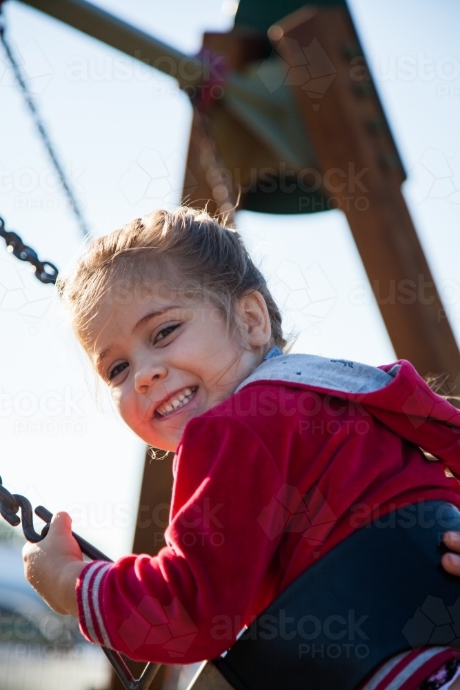 Image of Cute little girl in jumper swinging in park Austockphoto