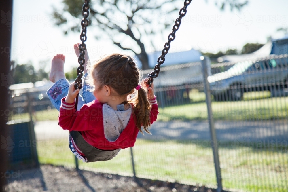 Cute little girl in jumper swinging in park - Australian Stock Image