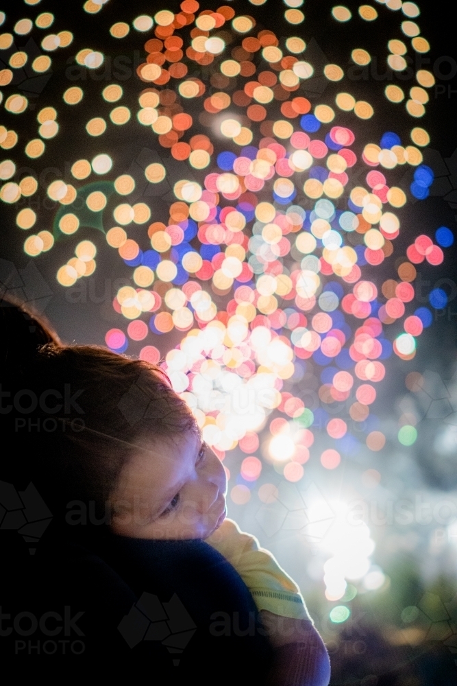 Cute mixed race baby boy cuddles his parent while new year's fireworks explode in background - Australian Stock Image