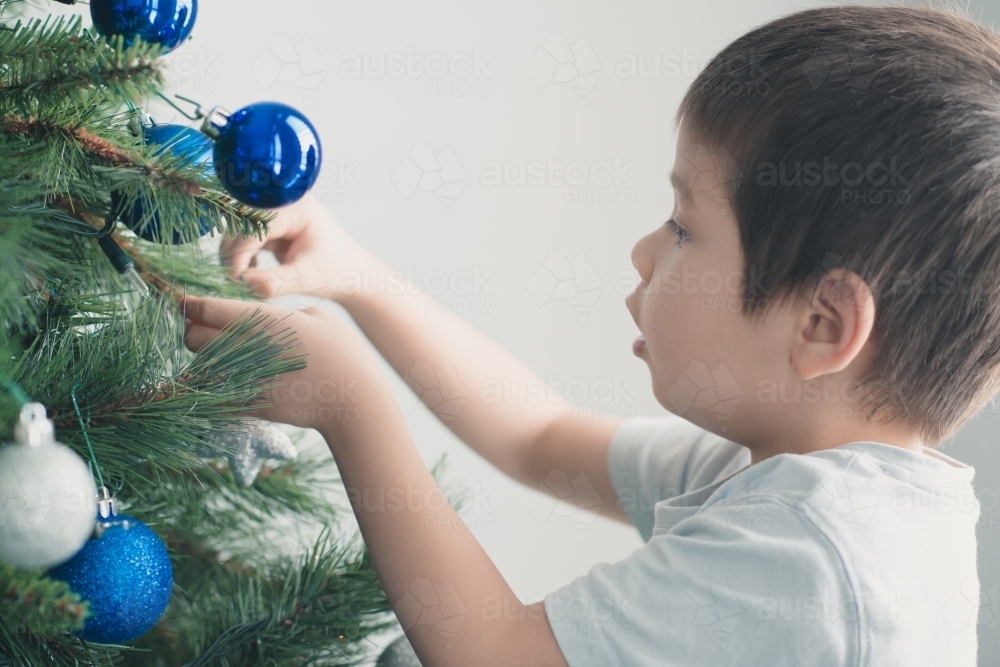 Cute mixed race boy hanging decorations on Christmas tree - Australian Stock Image