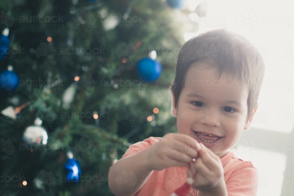 Cute mixed race boy hanging decorations on their Christmas tree - Australian Stock Image
