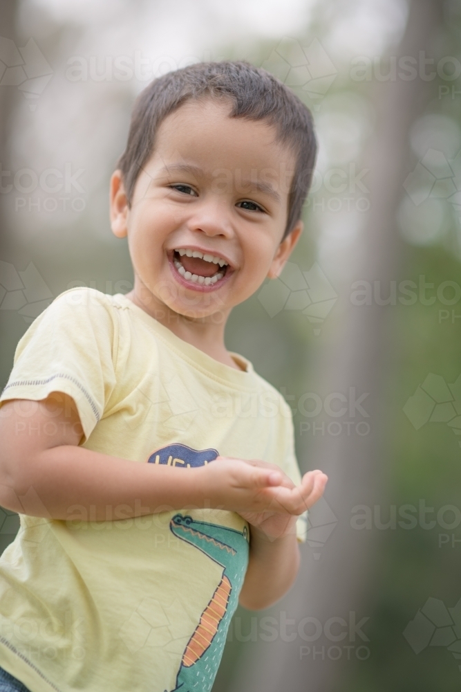 Cute mixed race boy playing in a park outside among the trees - Australian Stock Image