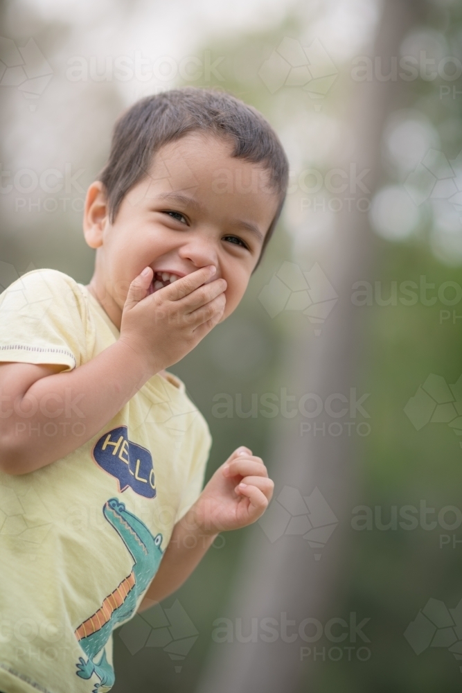 Cute mixed race boy playing in a park outside among the trees - Australian Stock Image