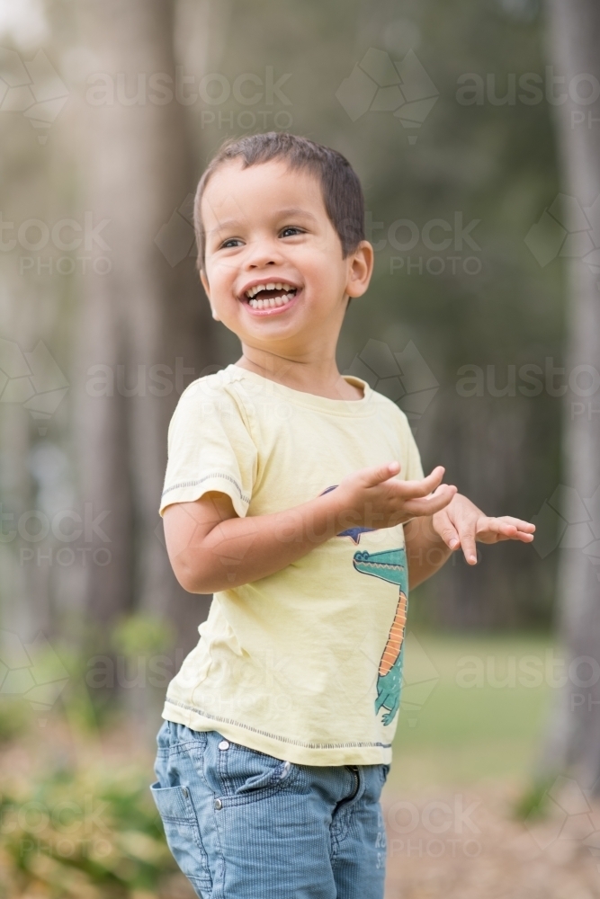 Cute mixed race boy playing in a park outside among the trees - Australian Stock Image