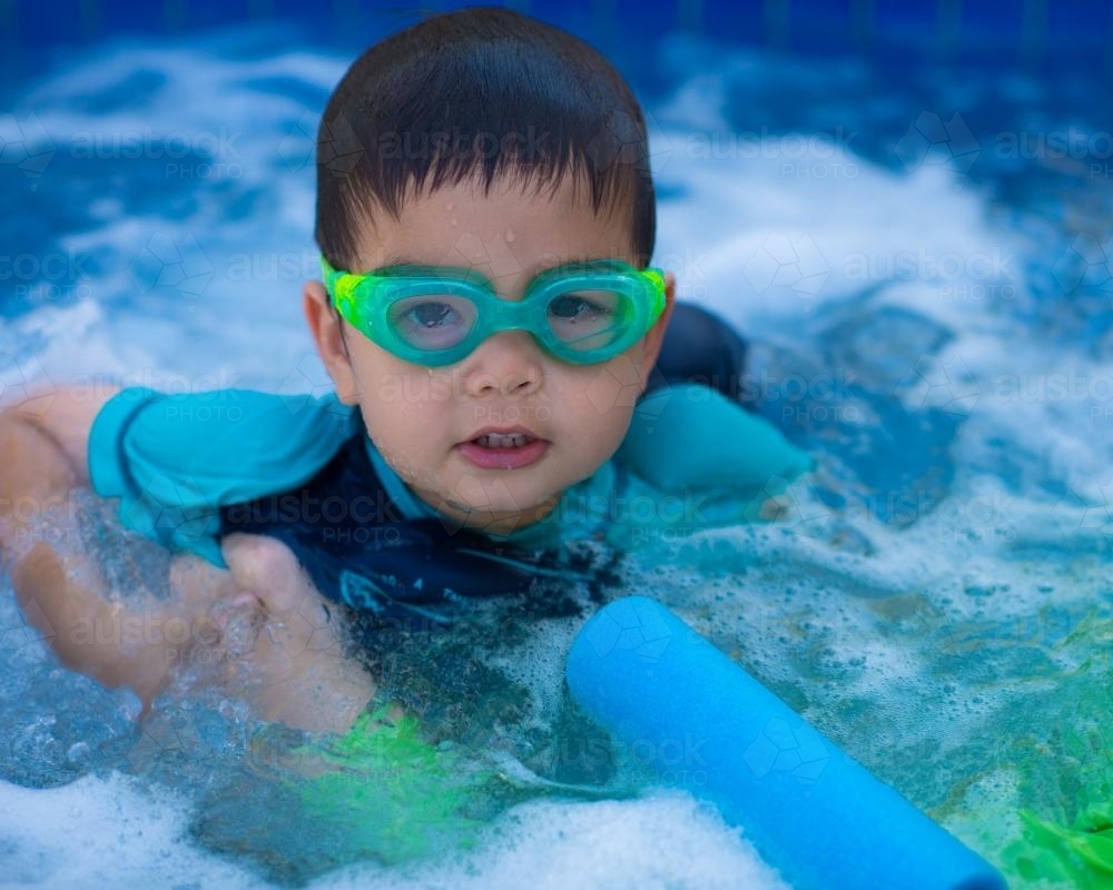 Cute mixed race boy plays in the bubbles of a backyard spa - Australian Stock Image