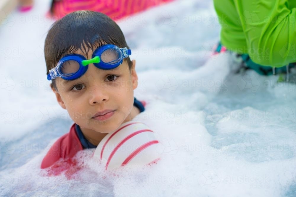 Cute mixed race boy plays in the bubbles of a backyard spa - Australian Stock Image
