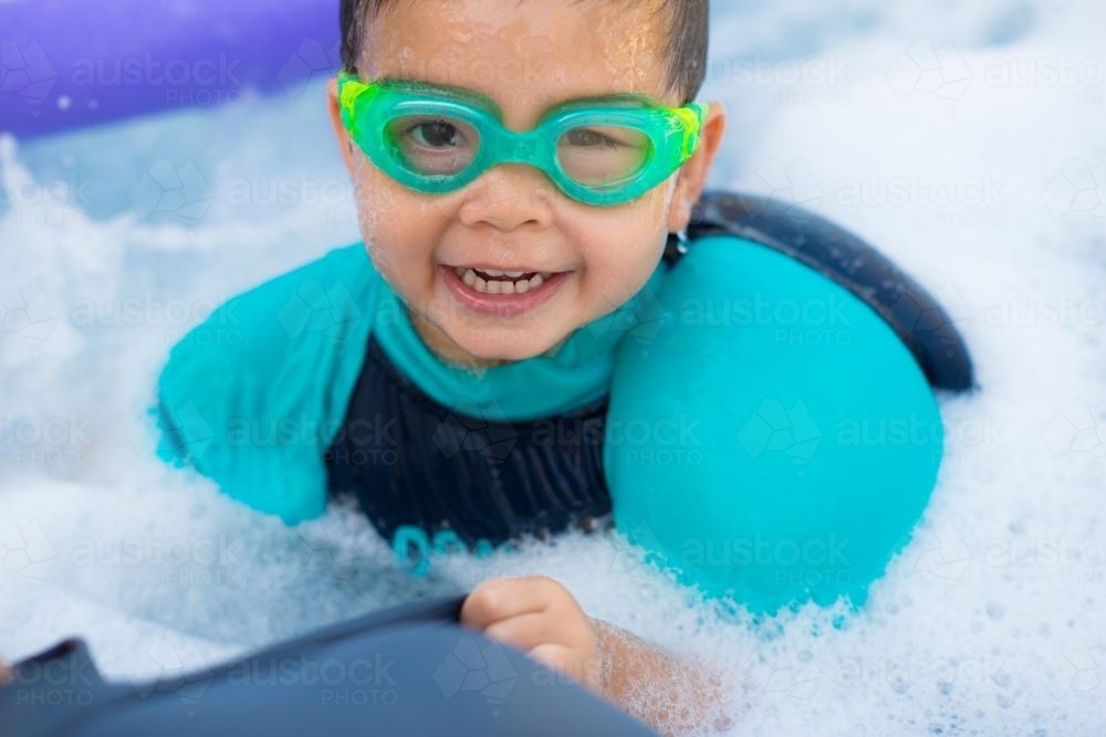 Cute mixed race boy plays in the bubbles of a backyard spa - Australian Stock Image