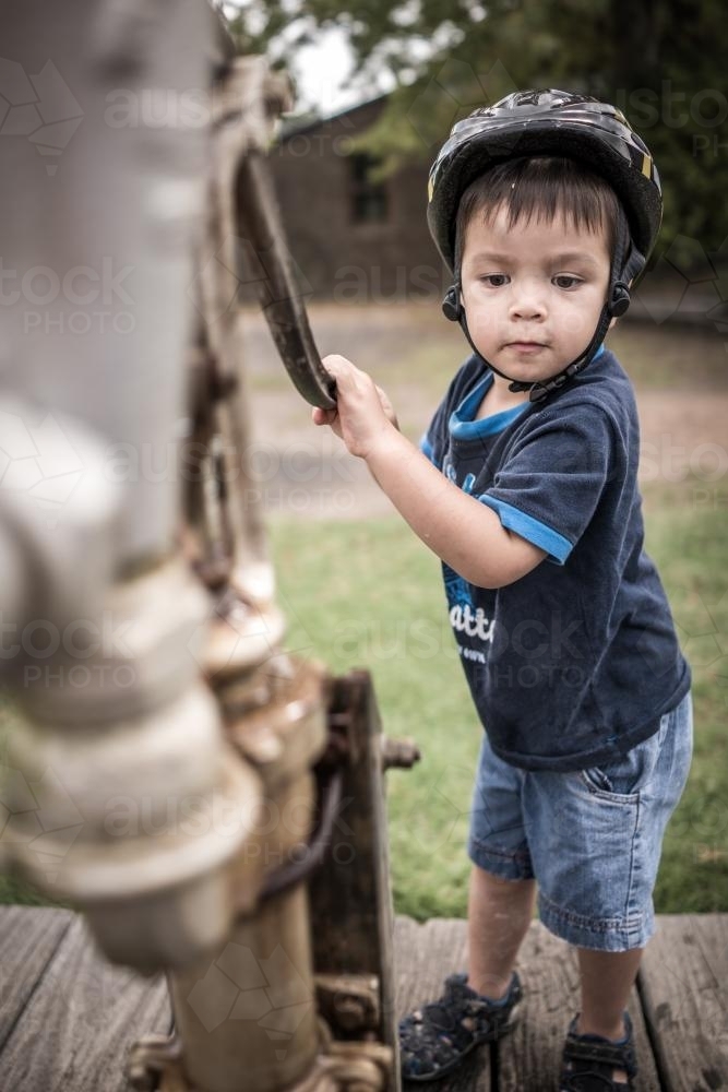Cute mixed race boy pumps water from an antique water pump - Australian Stock Image
