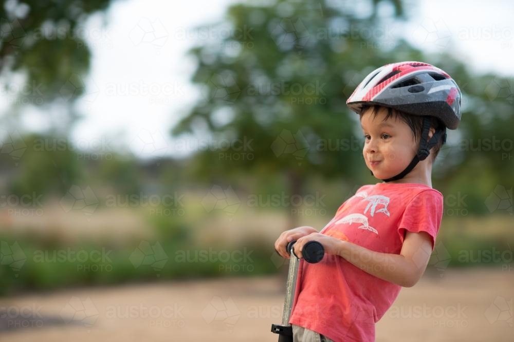 Cute mixed race boy wearing a helmet and riding his scooter - Australian Stock Image