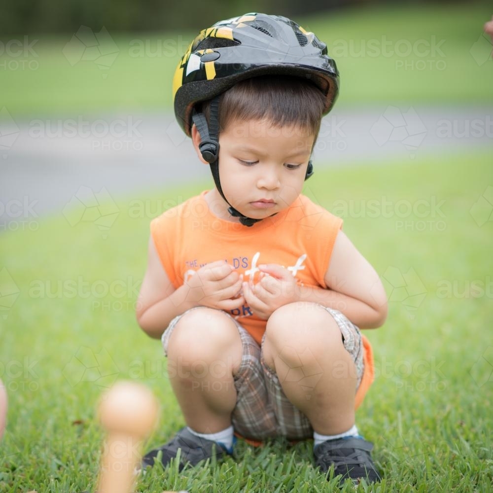 Cute mixed race boy wearing a helmet squatting on the ground - Australian Stock Image
