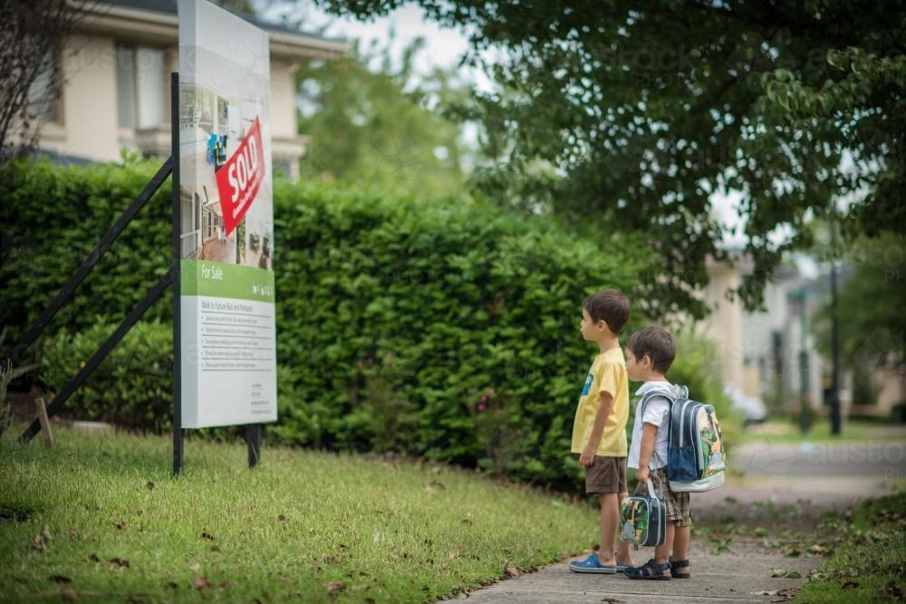 Cute mixed race brothers look at the sold sign in front of their suburban Sydney home - Australian Stock Image