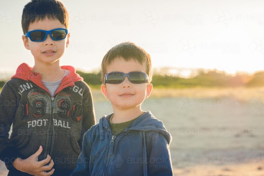 Cute mixed race brothers play together on a beach on a sunny winter day - Australian Stock Image