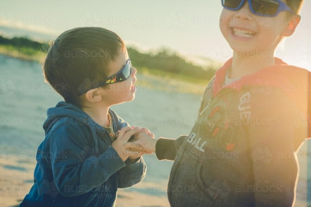 Cute mixed race brothers play together on a beach on a sunny winter day - Australian Stock Image