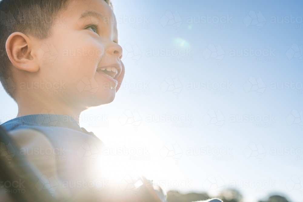 Cute mixed race three year old boy playing on a swing in a suburban playground - Australian Stock Image