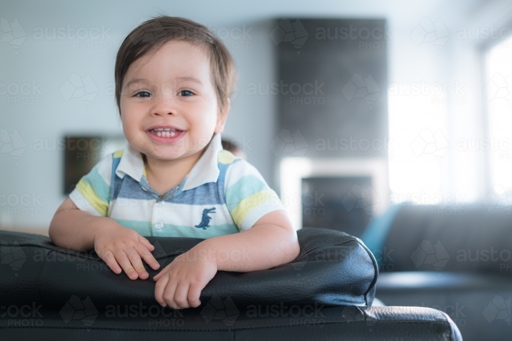 Cute mixed race toddler plays on a black leather lounge at home - Australian Stock Image