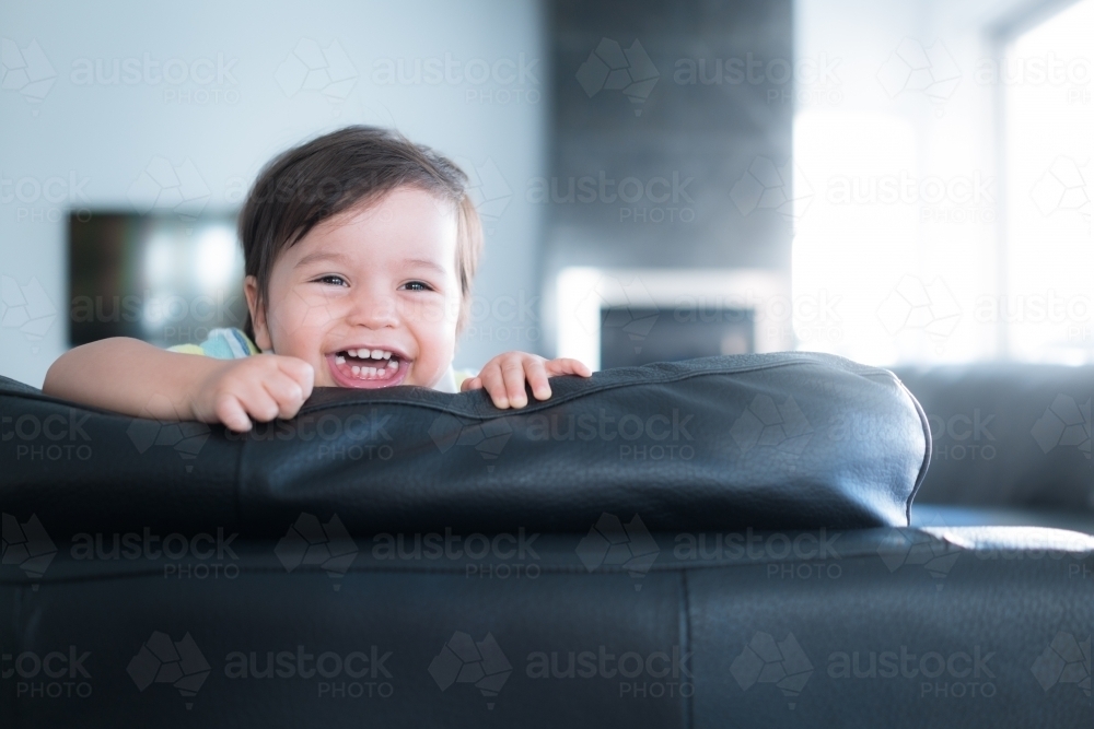 Cute mixed race toddler plays on a black leather lounge at home - Australian Stock Image