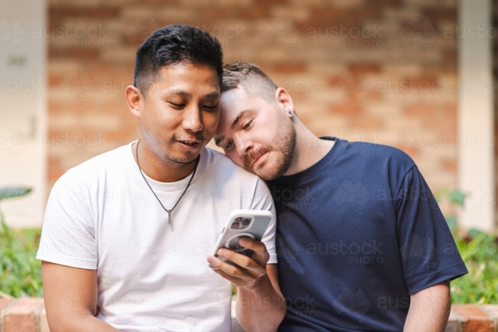 cute moment as gay couple look at phone screen - Australian Stock Image