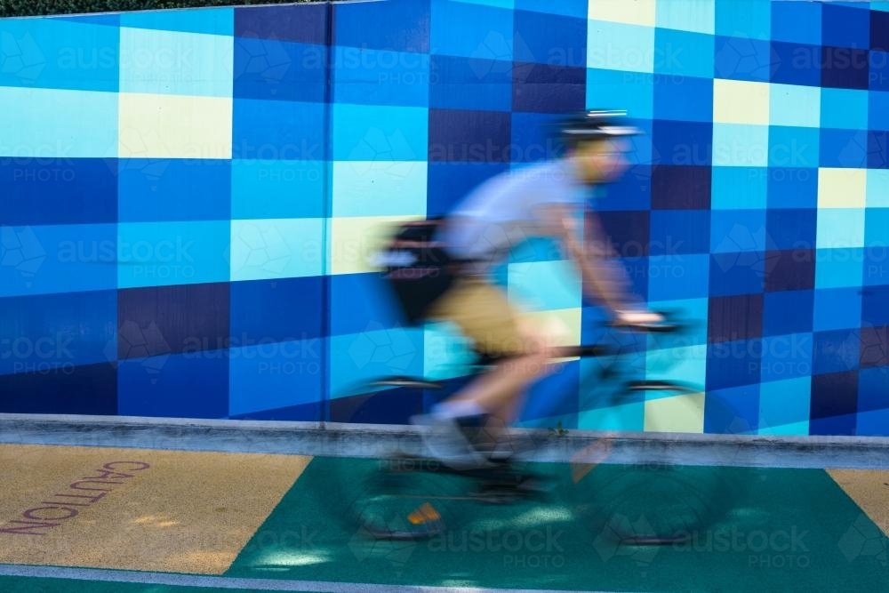 Cyclist blurred against blue tiled background - Australian Stock Image